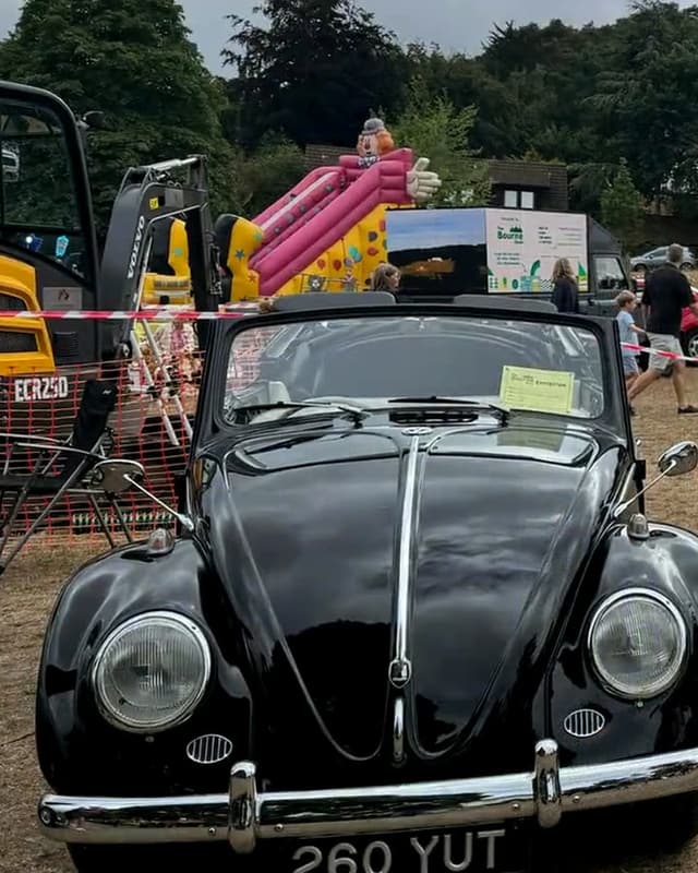 Our black VW Beetle on the grass at the Bourne Show, with a fairground slide behind