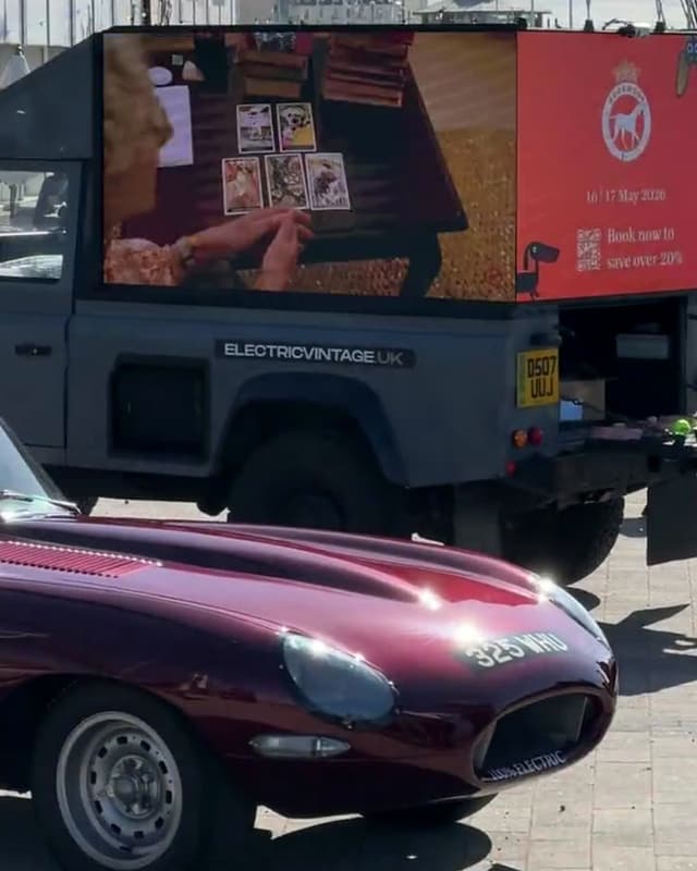 Our maroon E-Type parked in front of a grey AdRover with its screen lit on Brighton seafront